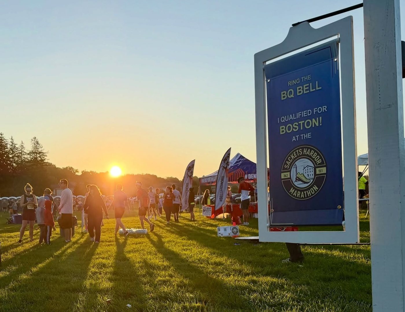The Ring the BQ Bell sign in the finish area, backlit by sunrise over the field
