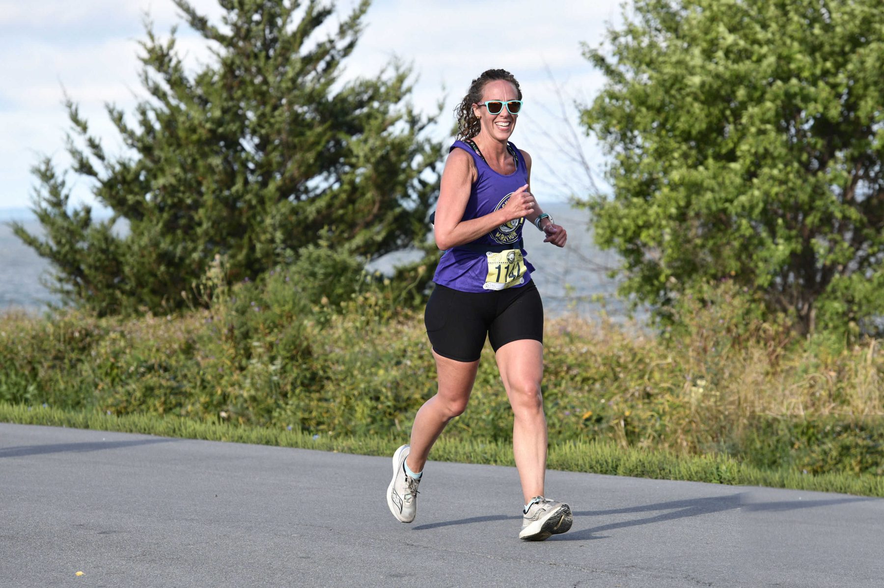 A smiling runner in a purple singlet on the lakeside course, Lake Ontario behind the trees