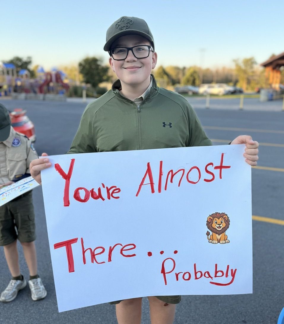 A young spectator holding a sign reading You're Almost There... Probably